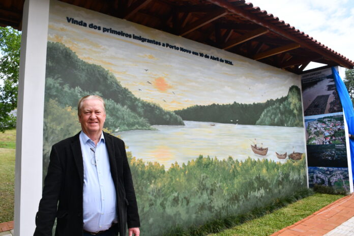 2 Inácio diante do painel que retrata a chegada dos pioneiros a Porto Novo pelo Rio Uruguai